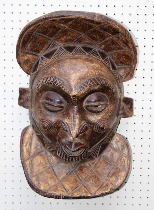 A 20th century carved wood African tribal mask with pursed mouth, lozenge pattern headdress and