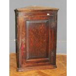 A George III oak wall mounting corner cupboard of small size, the fielded panel door enclosing three