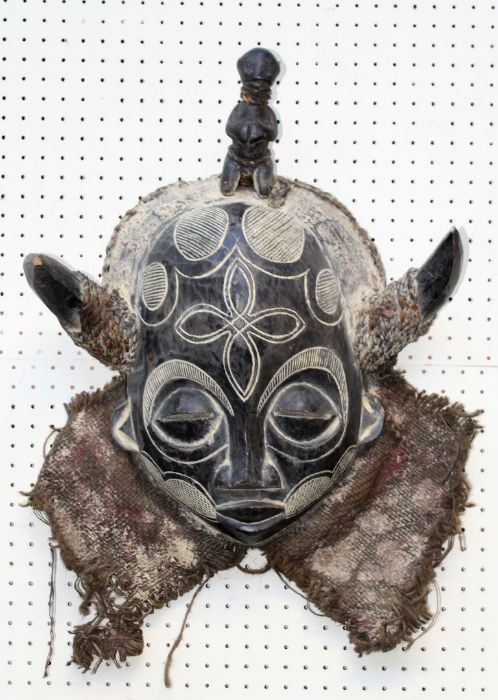 A 20th century carved wood African Tribal mask, with horns, closed eyes and woven cloth collar,