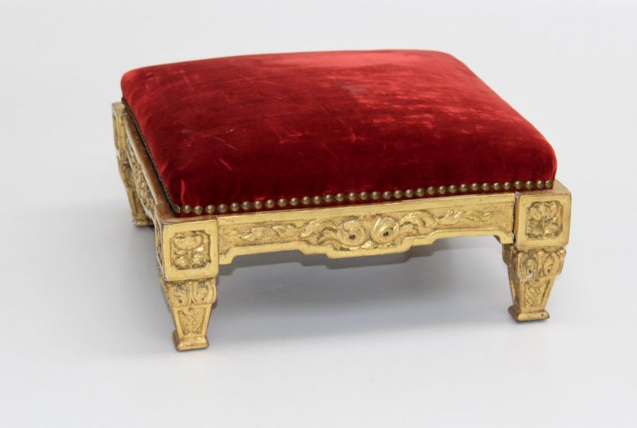 A 19th century carved giltwood footstool, the close studded red plush upholstered pad over rose