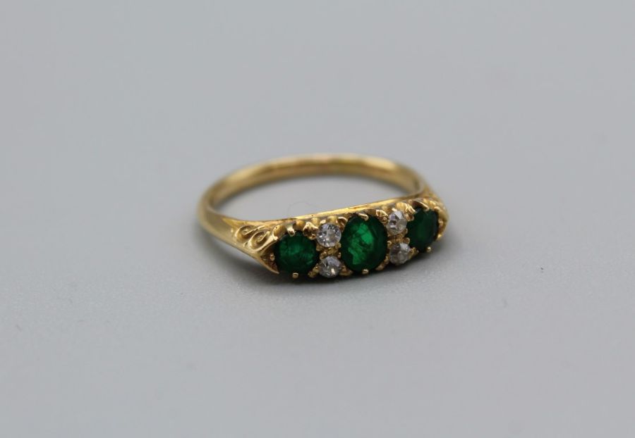 An Edwardian three stone emerald ring. The principal stone approximately 4mm diameter, the