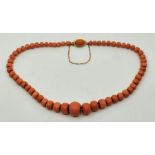 A salmon pink faceted graduated coral bead necklace, probably Italian, with 18ct. yellow gold