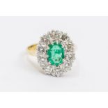 An emerald and diamond cluster 18ct gold ring, comprising an oval emerald set to the centre,