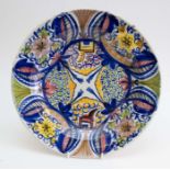 A Dutch style Delft polychrome charger, decorated with chairs, flowers and foliage, signed T.B to