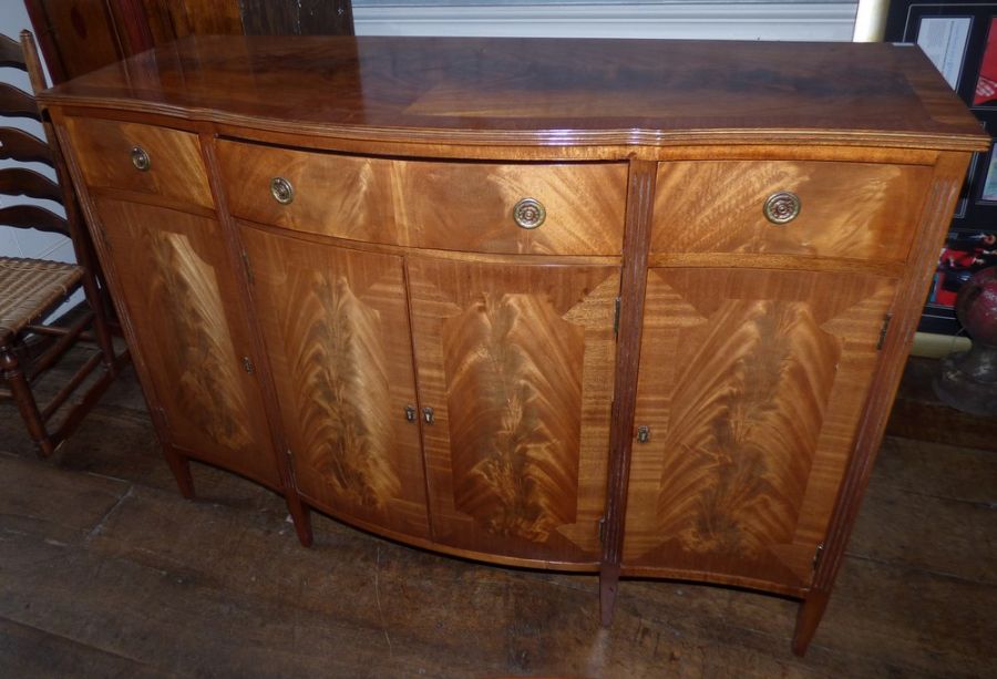 A George III style flamed mahogany sideboard, serpentine outline with fluted edge, above three