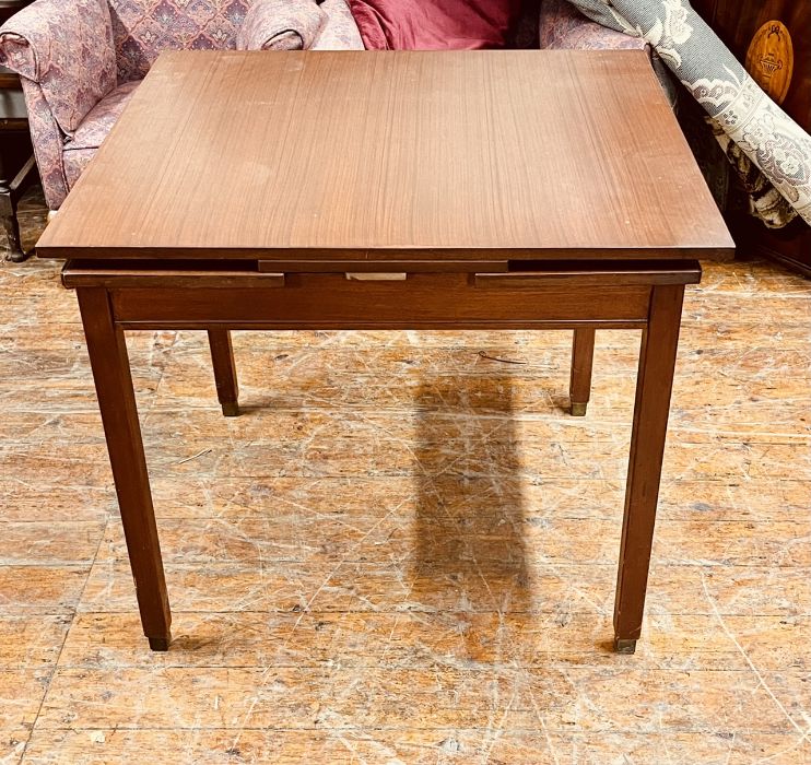 A mid 20th century dark teak drawleaf extending dining table, raised on square supports on brass