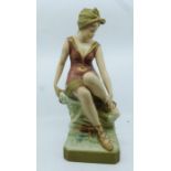 A large Royal Dux figure of a dancer painted in typical palette, she sits on a rocky plinth