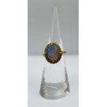 An opal cocktail ring, in an unmarked yellow setting. The opal is en cabochon and has a blue-green