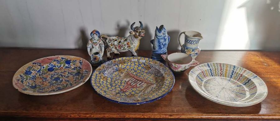 Three polychrome tin glazed chargers, a jug, bowl, a faience vase modelled as a cow, a faience