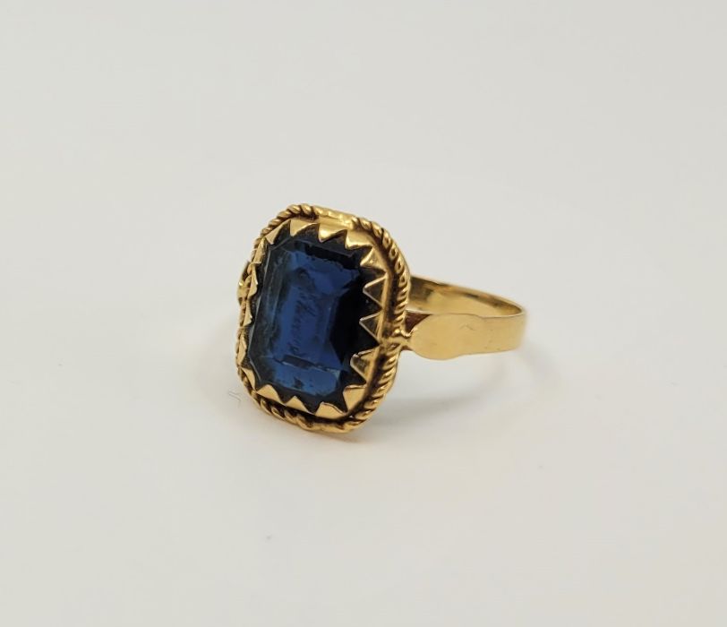 A precious yellow metal and blue paste set cocktail ring, claw set emerald cut blue paste to