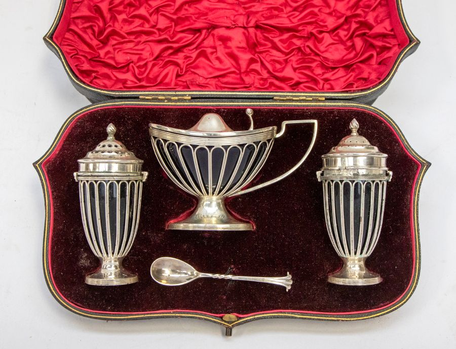 An Edwardian Neo-Classical style silver three piece condiment set to include boat shaped mustard pot