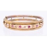 An early 20th century ruby and diamond set yellow metal bangle, comprising a row of alternate