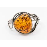A silver and amber set bangle, comprising a large irregular shaped clarified amber approx 38mm,
