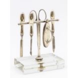 A novelty George V silver manicure set on glass base, to include; nail buffer, steel scissors and