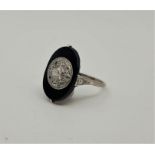 A precious white metal, black onyx and diamond ring, having central circular mount set old-cut