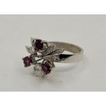 A 14ct. white gold, diamond and ruby ring, having leaf clusters set round cut diamonds and three