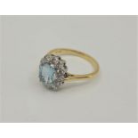 An 18ct. gold, aquamarine and diamond ring, with central emerald cut aquamarine bordered by twelve