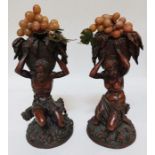 A pair of hard wood carved sweetmeat table centres, one male one female carrying baskets on their