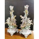 A pair of continental Dresden style candlesticks modelled with maidens in horse drawn chariots and
