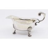 A George V silver sauceboat with leaf designed handle and shell like shaped feet, hallmarked London,