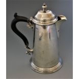 A Georgian style silver hot water jug, the hinged domed cover with turned finial, fruitwood scroll