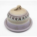 A studio pottery cheese dish with a twisted floral designed handle and purple and grey floral design