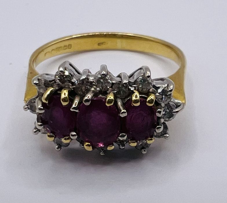 An 18ct gold Ruby and diamond cluster ring. featuring three mixed cut, oval shape rubies and 16