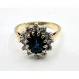 An 18ct gold Sapphire and diamond cluster ring. Featuring an oval mixed cut sapphire in dark blue,