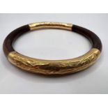 A bamboo and yellow metal bangle. The gold metal is adorned with pictures of bamboo in leaf.