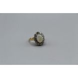 An opal and diamond cluster ring, set with a central cabochon of white opal, with greenish play of