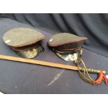 Two East German postal hats, along with a wall hanging sword