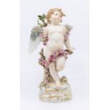 A Meissen figure of a weeping cherub wrapped in a flower garland and reclining by a tree. Date is