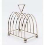 An Arts & Crafts silver seven bar toast rack, arched shaped wire work racks on four ball feet,
