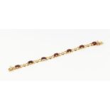 A 9ct gold garnet set bracelet, set with seven oval mixed cut garnets interspersed with gold bows.