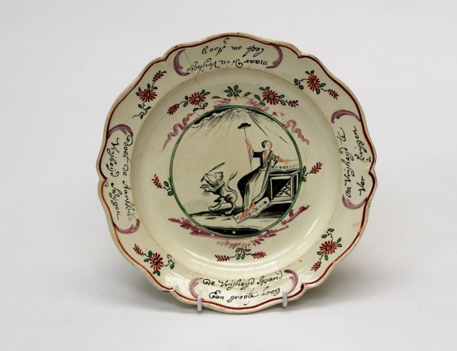 An 18th century Dutch decorated creamware plate with lion holding sword and arrows beside a seated