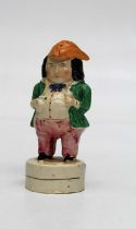 An early 19th century creamware sander fashioned as a toper wearing a tricorn hat, with ale jug