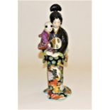 A Japanese Kutani geisha carrying a small child, 36.5cm high and a similar figure holding a bowl,