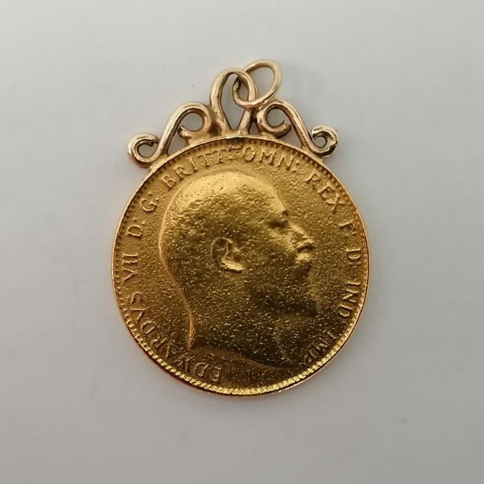 An Edward VII 1910 sovereign with soldered yellow metal scroll mount. Approximate weight 8.4 grams.