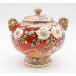 An early 20th century Japanese Satsuma urn and cover decorated with flowers and butterflies on a red
