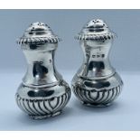 A pair of sterling silver pepperettes, oval outline with fluting from the footed base and