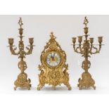 A brass mantle clock along with matching pair of candelabra, all decorative with cherub and gilt