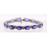 A Tanzanite and diamond set line bracelet. Set with fourteen mixed oval cut  dark violet-blue