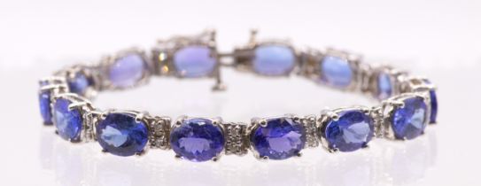 A Tanzanite and diamond set line bracelet. Set with fourteen mixed oval cut  dark violet-blue