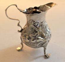 A George III pear shaped cream jug repousse with bird, fruit and foliate scrolls, scroll handle,