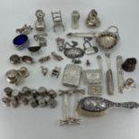 A selection of mainly silver items to include charms, brush, tongs, salt, furniture, thimbles and