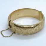 A 9ct gold hinged bangle. Marked for Birmingham 1963. With foliate engraving on the outside. Gross