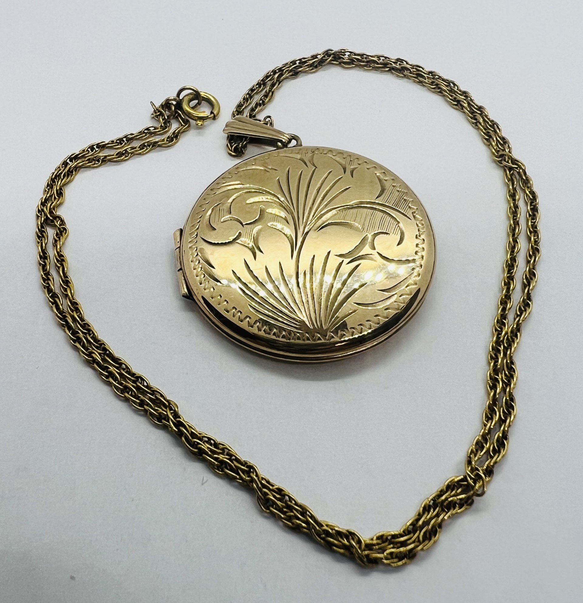 A 9ct circular locket with foliate engraving on a "9ct" stamped chain. Gross approximate weight 9.