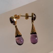 A pair of amethyst drop earrings. Featuring a yellow metal bezel set cabochon in each stud, with a