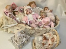 A collection of Modern porcelain baby dolls in a large woven baby bassinet, and Ashton Drake