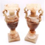 A pair of alabaster urns and covers with twin scroll handles, the covers with shaped borders, square
